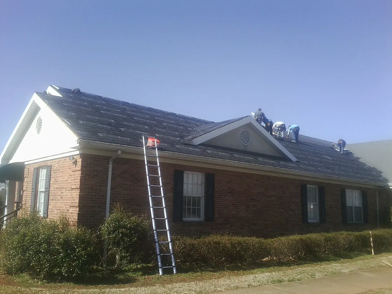 Crew tearing shingles off a brick ranch roof with a ladder set — Emergency Roof Repair work by our crew in Cheney