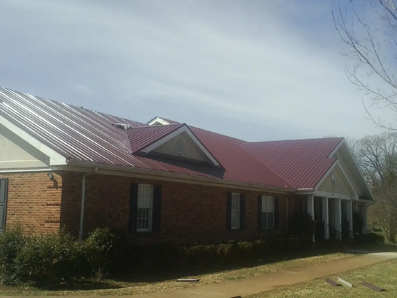 Red metal roof with gabled entries on a long brick building, from a Hail Damage Roof Repair job in Cheney