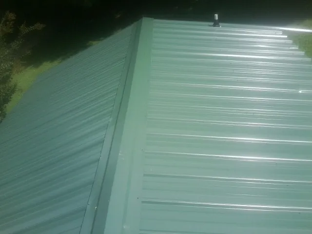New green metal panels meeting at the ridge of a roof — Flat Roof Repair work by our crew in Cheney