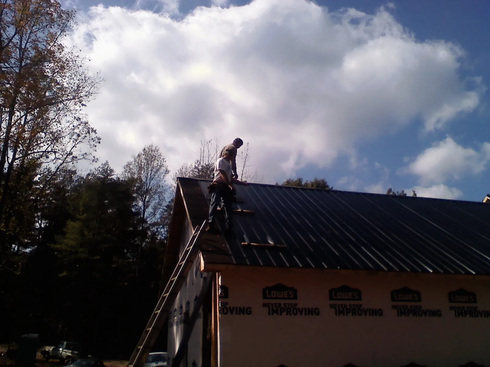 Roofer fastening dark metal panels high against a cloudy sky, from a Roof Inspection job in Cheney